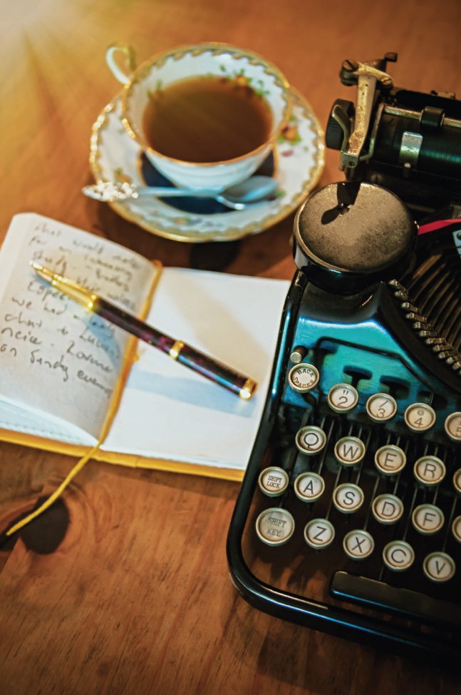 Eine Tasse Tee, ein Notizbuch mit Stift und Teil einer Schreibmaschine